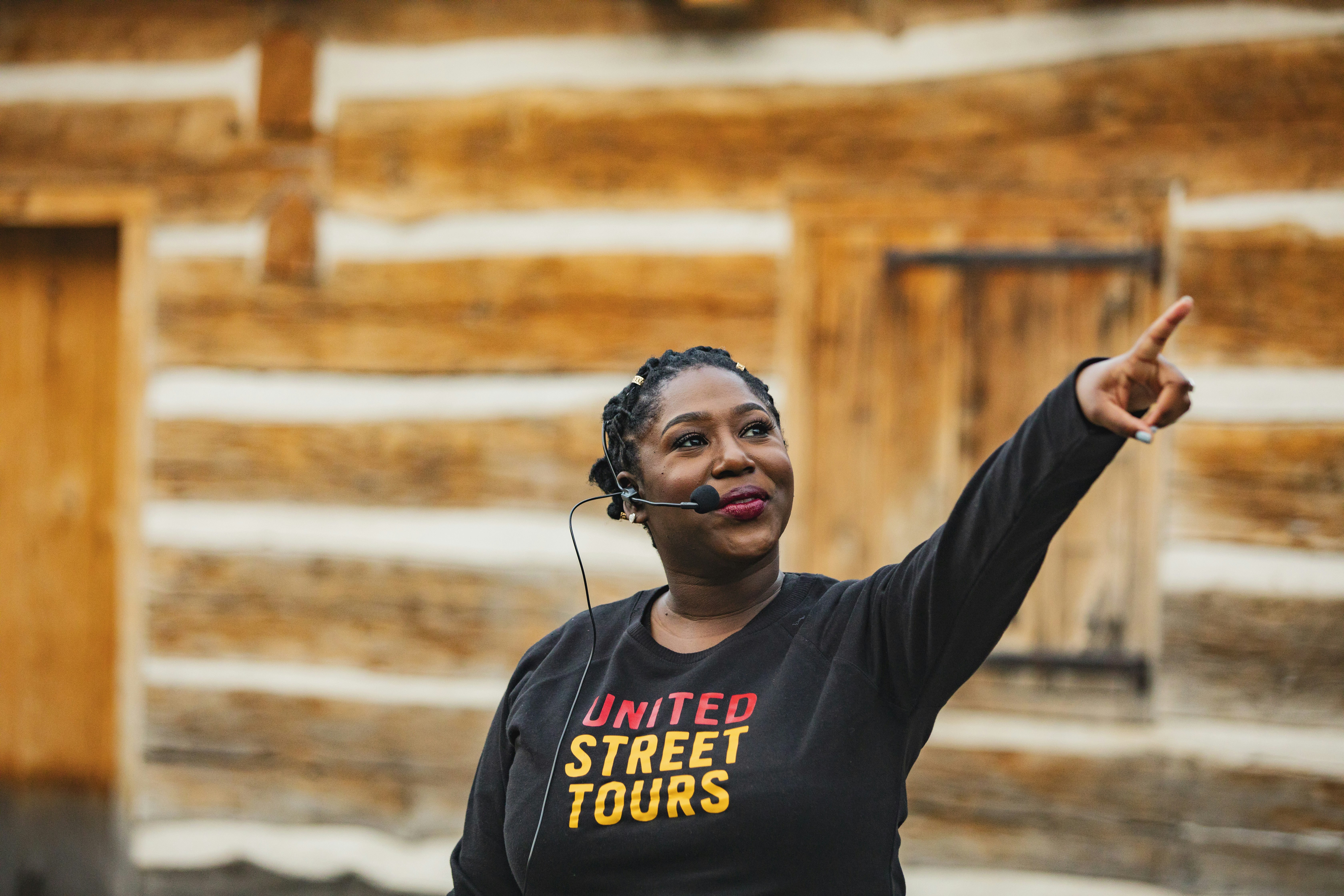 A woman wearing a head microphone and a black t-shirt that says 'United Street Tours' points to something out of frame.